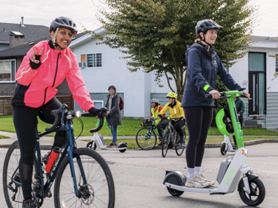 1 person on bike smiling and one person on scooter smiling riding down a neighborhood street