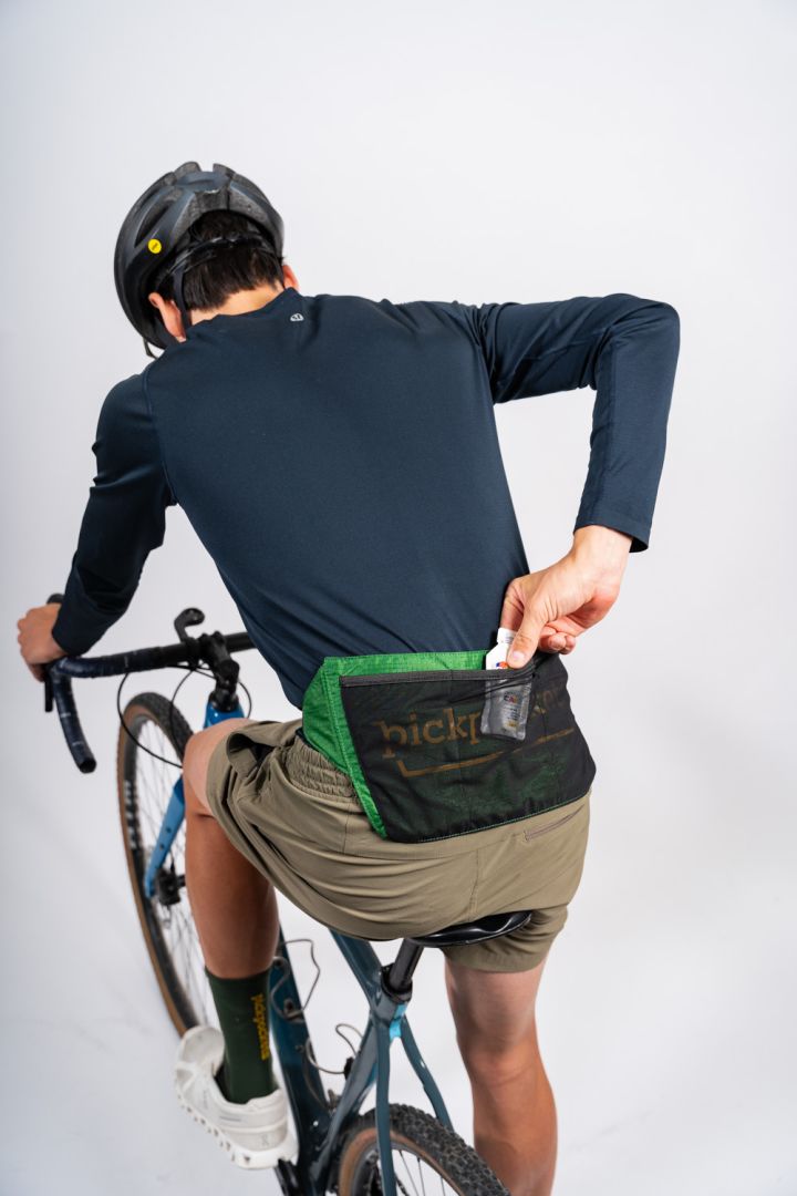 Male cyclist wearing a green pickpockets activity belt putting a snack in the belt while riding