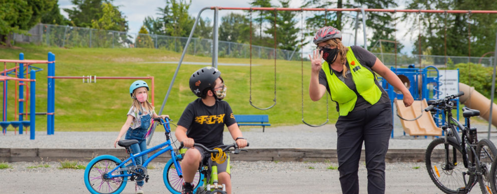 A bike education instructor holds up four fingers as a student looks over his shoulder to see how many fingers she is holding up.