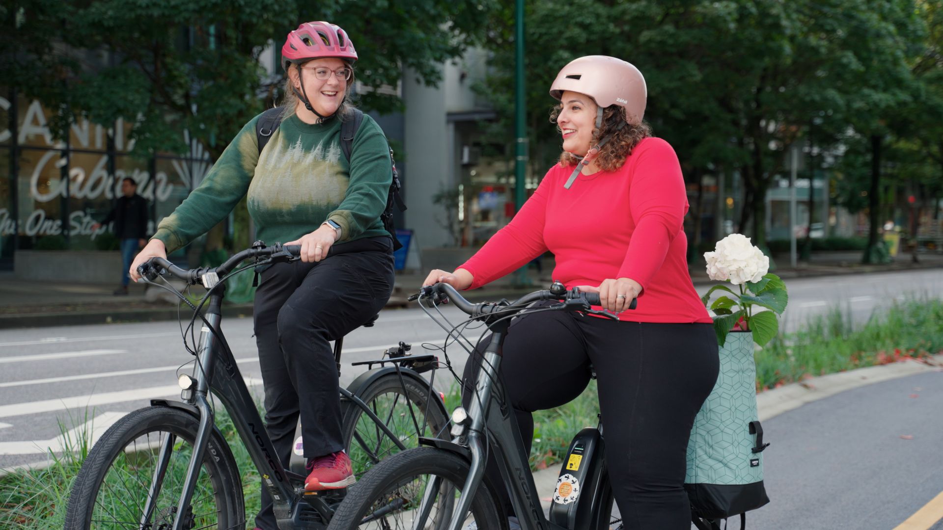 Two women smile next to each other on e-bikes