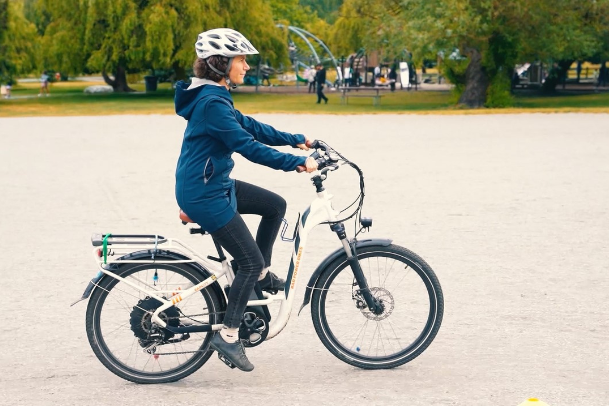 A woman rides an e-bike on a gravel field.