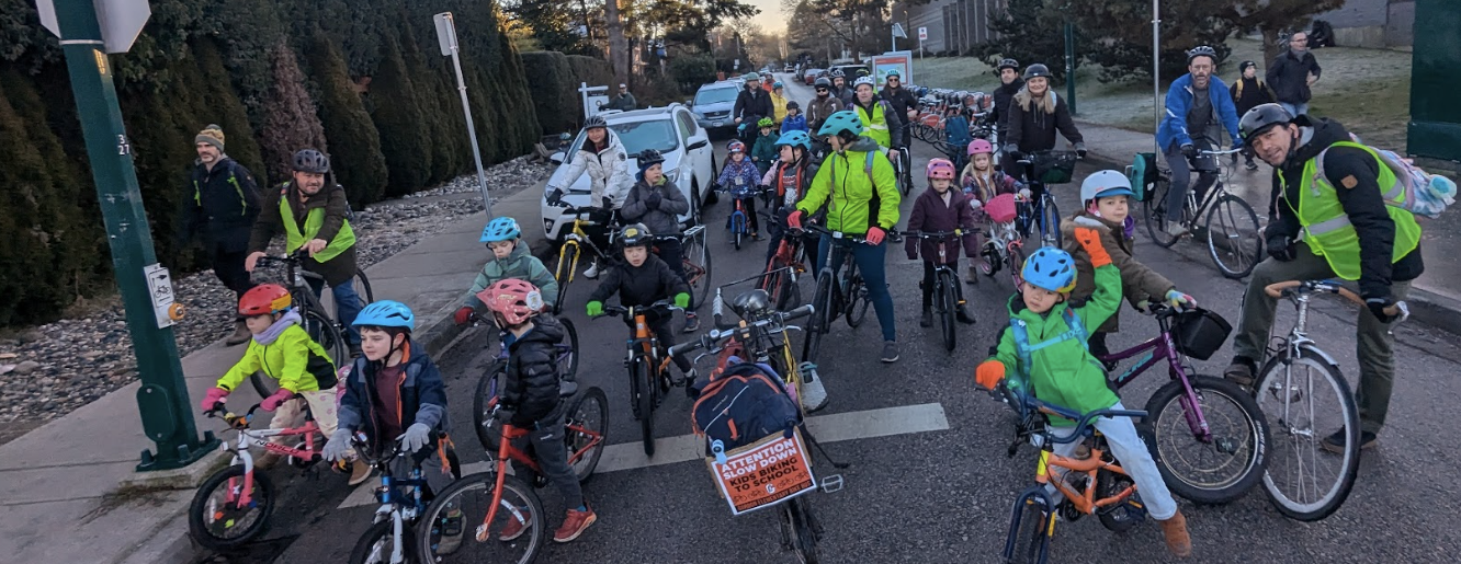 A group of students and parents stop at a stop sign on a residential street. They are riding their bikes to school in a 'bike bus'.