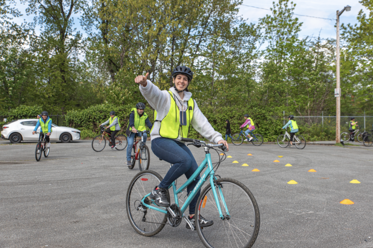 A woman is riding a bike and gives a thumbs up. She is smiling.