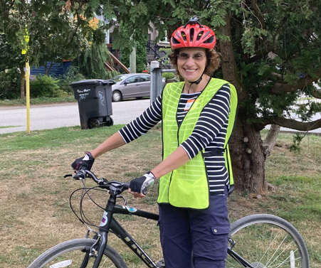 Roberta Walker, a woman in her 60s, stands with her bike. She is wearing a yellow vest and a red helmet.