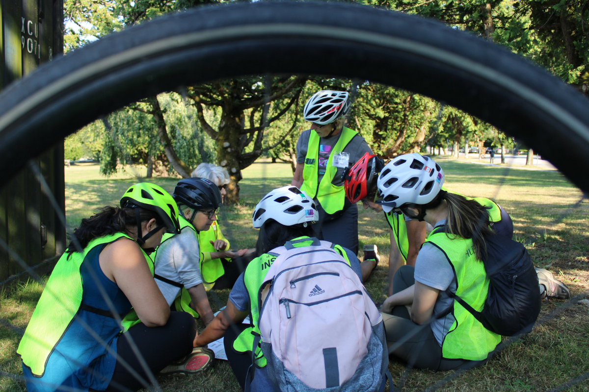 A group of women and an instructor huddle around on the grass.