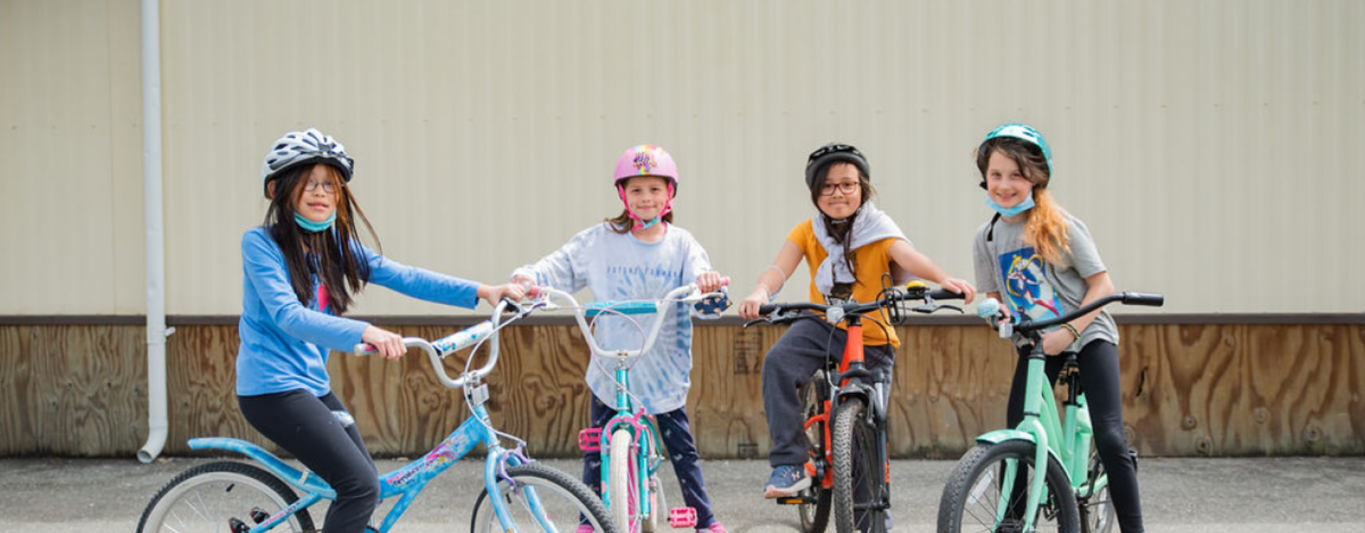 Four girls stand with their bikes on school grounds.