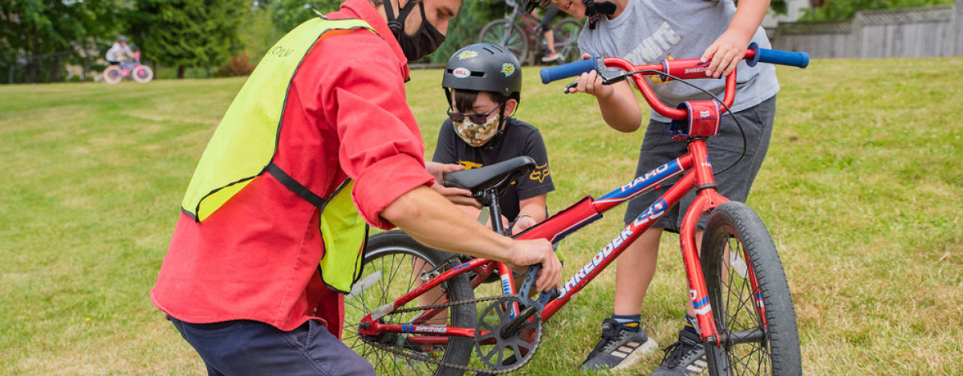 A bike instructor inspects a bike with two students.