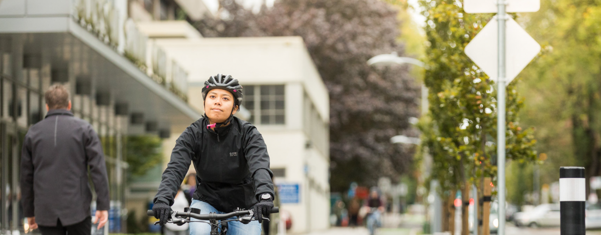 An Asian woman in her 20s rides her bike on a separated bike lane in Vancouver.