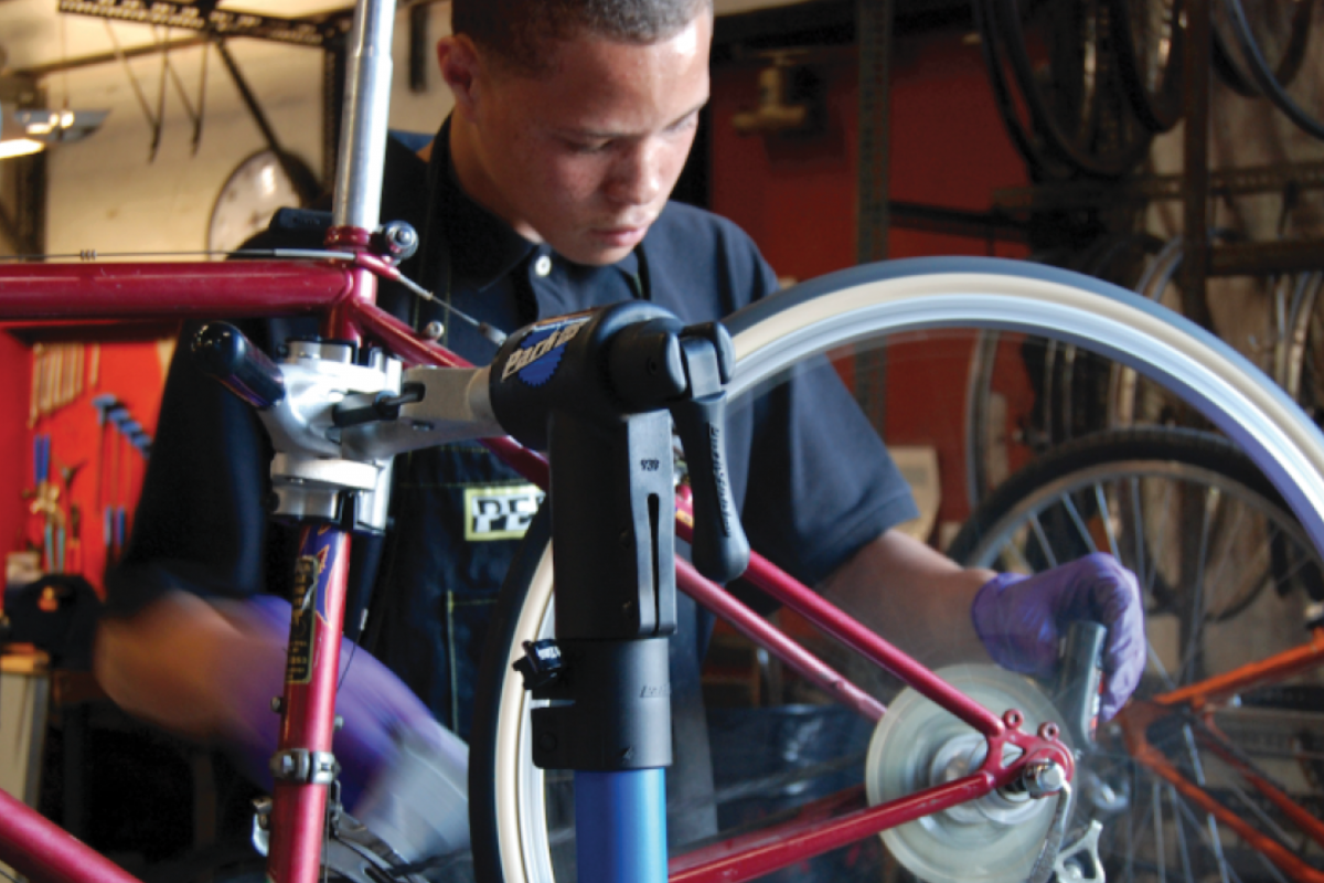 A young male-presenting bike mechanic is fixing a rear bike wheel. He looks deep in concentration.