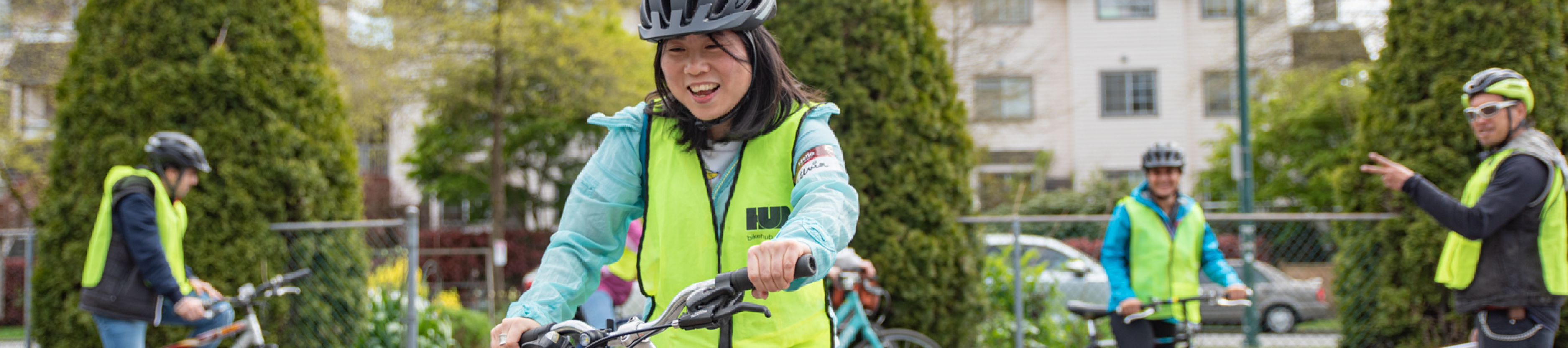 A middle-aged Asian woman rides her bike on a gravel field. There are several other people riding bikes behind her.
