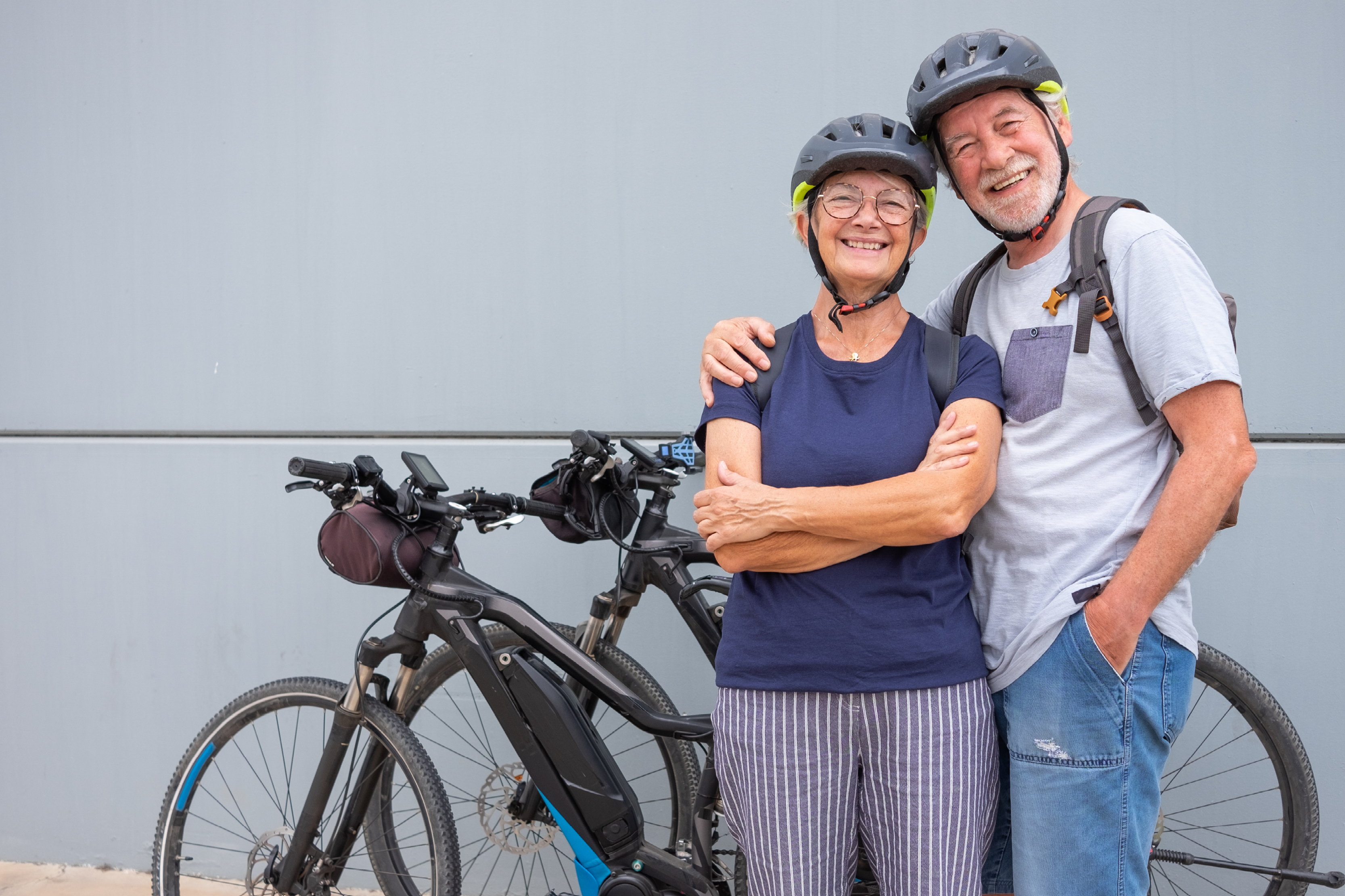 An couple in their 60s stand beside their two e-bikes and smile for the camera.