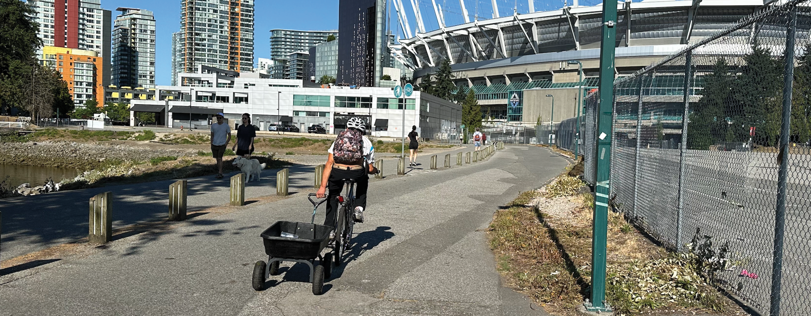 A person rides a bike on Vancouver's Seawall. They are holding on to the handle of a wagon as they ride.