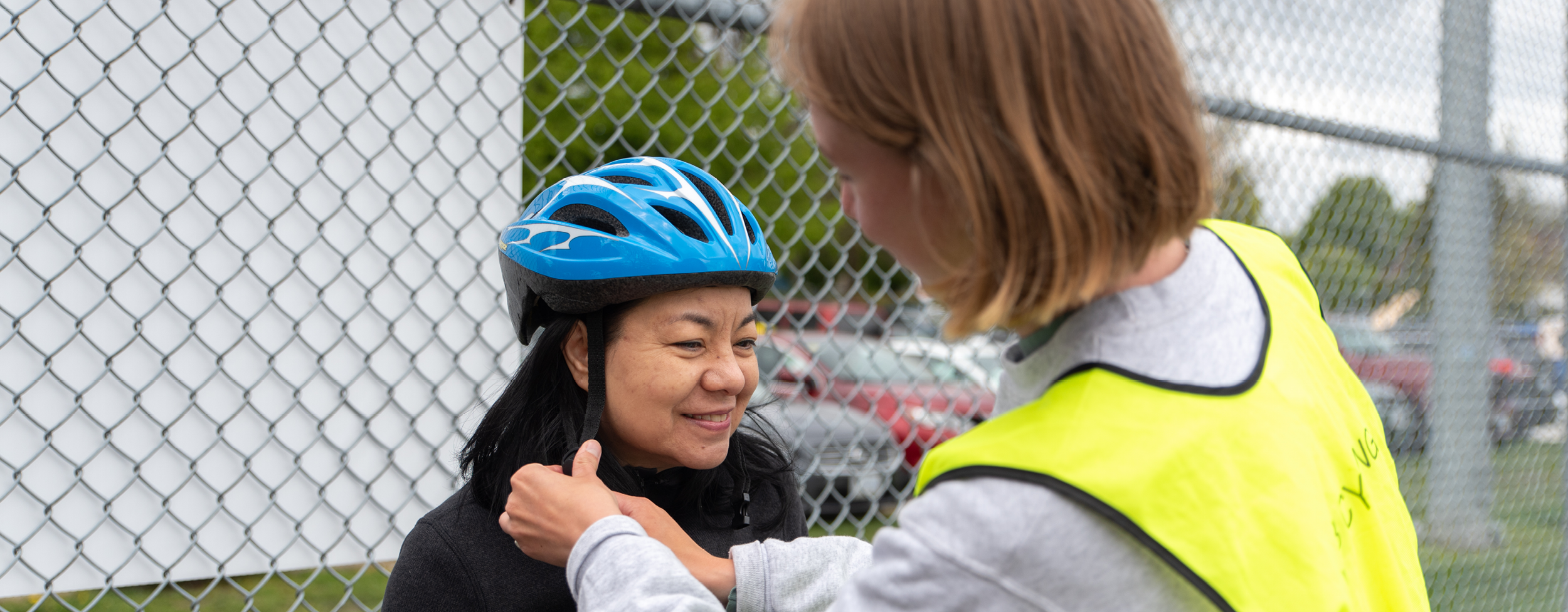 A bike education instructor helps fasten the helmet of an adult Asian woman in her 60s. She is taking a cycling education course.