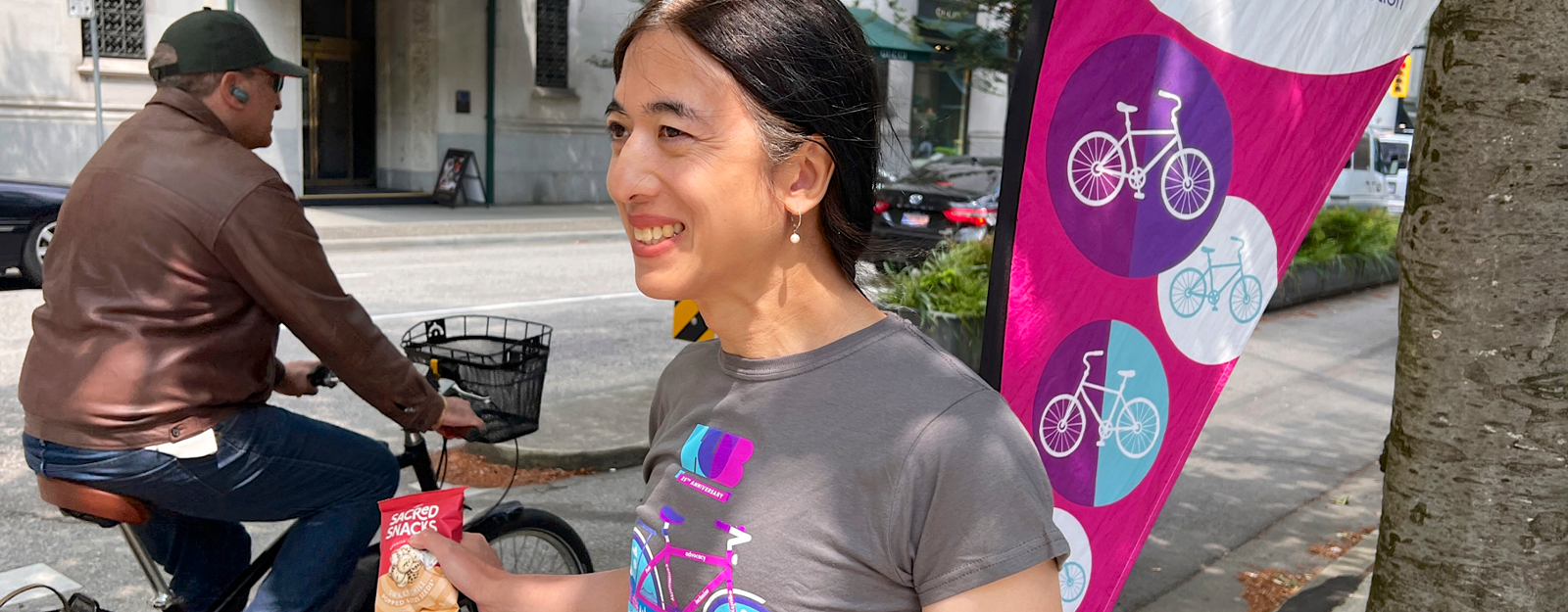 A woman hands out snacks along a bike path. She is wearing a HUB Cycling t-shirt.