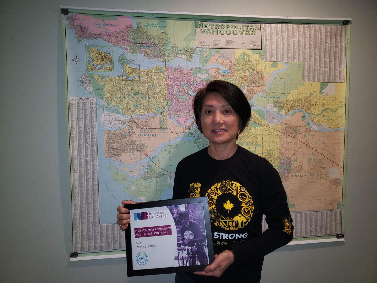 Donna Kwan, a member of Richmond's Local Committee wins a Volunteer Appreciation Award at HUB's Bike Awards. She is standing holding the award. There is a large map of Metro Vancouver on the wall behind her.