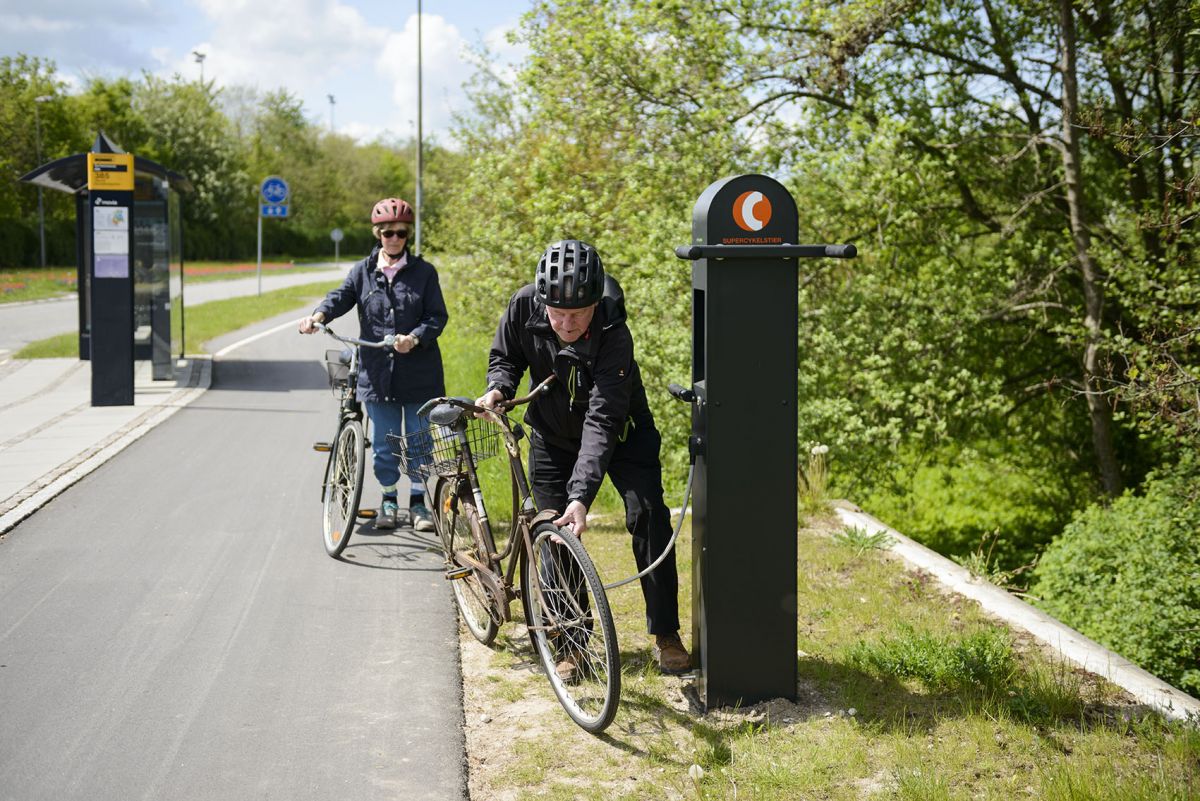 A senior man and woman stop riding along a cycle highway in the Capital Region of Denmark. The man fills up his front bike tire with air. Photo credit: Cycle Superhighways, Capital of Denmark
