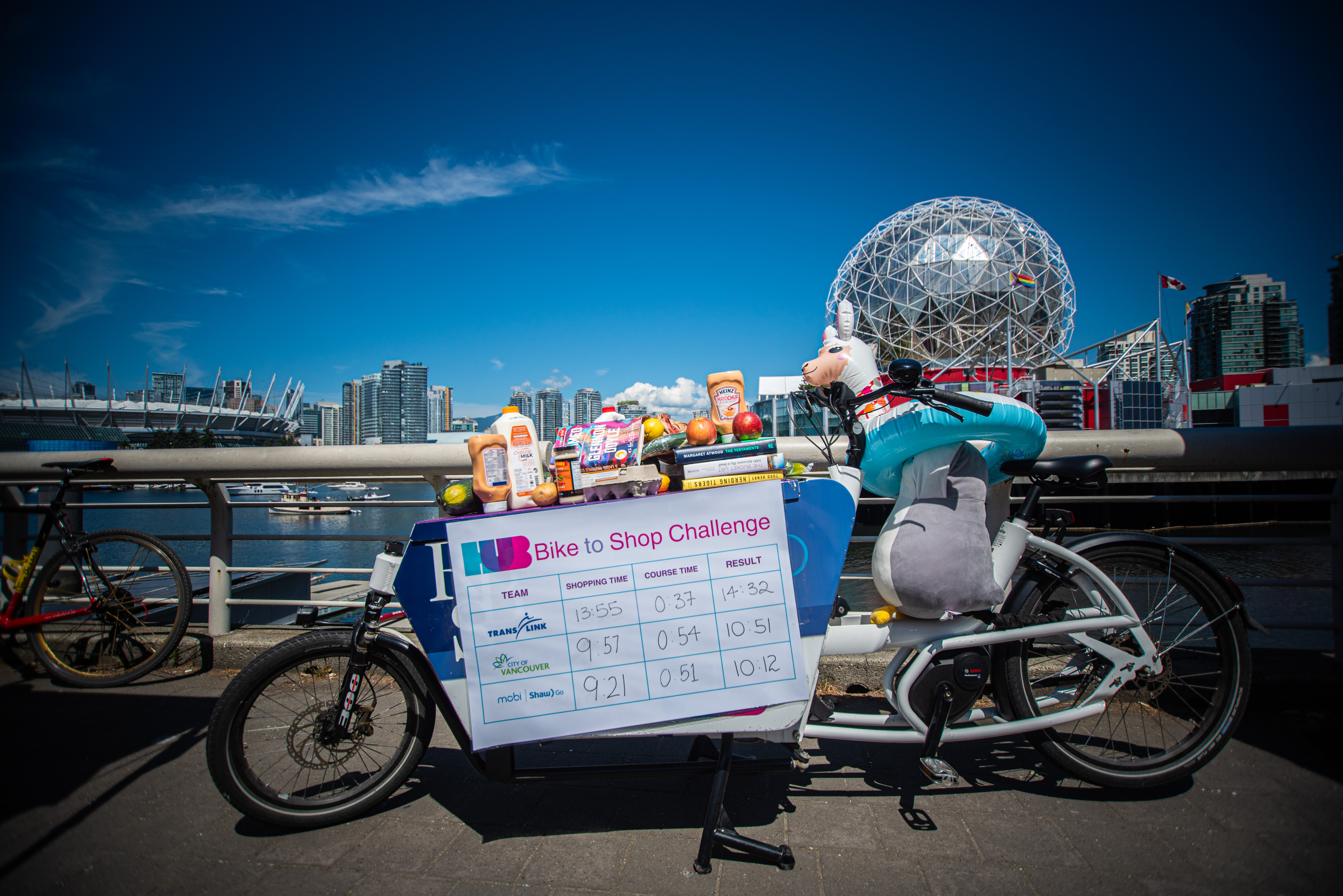 An image of the Bike to Shop Challenge scoreboard against HUB Cycling's e-cargo bike. Mobi by Shaw Go just sneaking in first place with a 10:12 finish time! The City of Vancouver took second place with a 10:51 finish time, followed by TransLink finishing at 14:32.