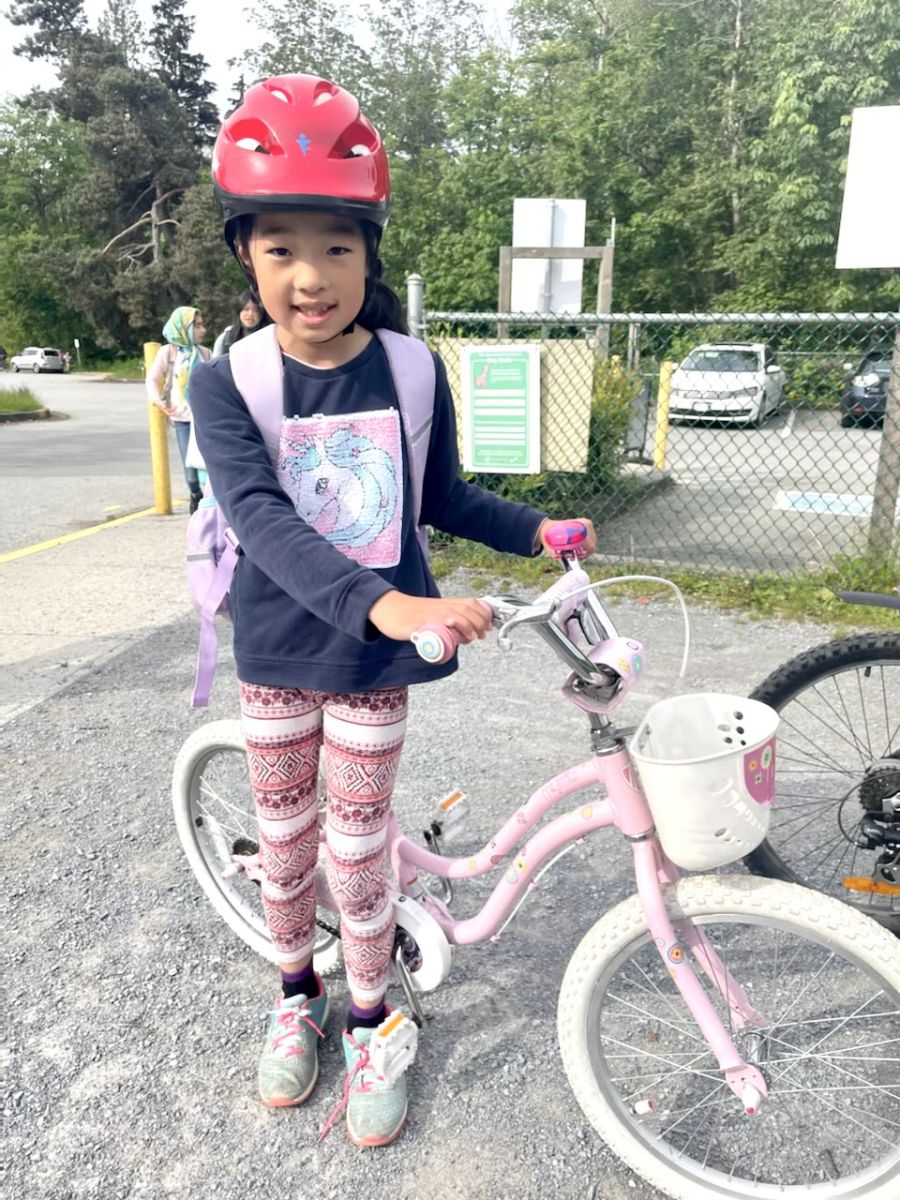 Eight year-old Emma stands beside her bike. She is wearing a red helmet, navy long sleeve shirt and patterned pink leggings. Her bike is baby pink with a small white basket at the front.