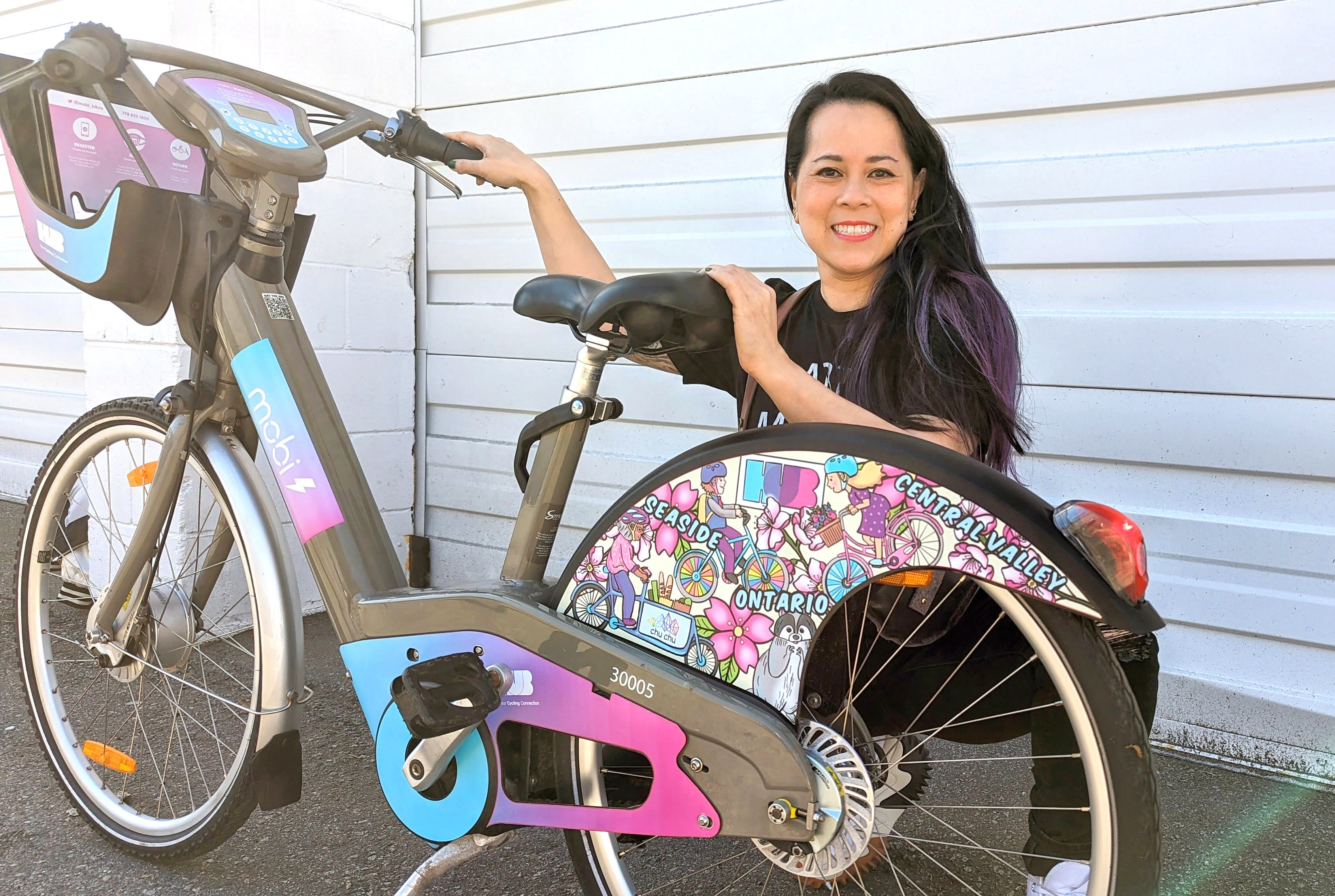 Serena Chu, a woman, poses with a new HUB Cycling x Mobi by Shaw Go bike. Serena designed the bike.