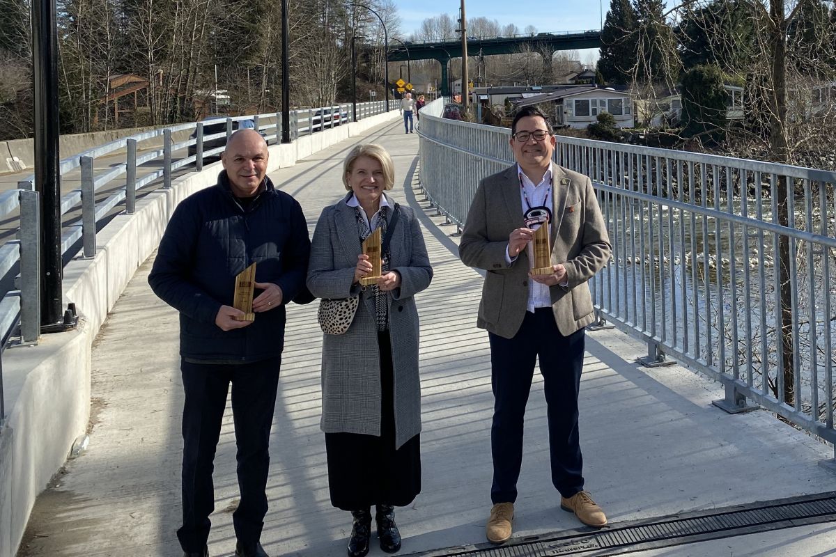 Representatives from the District of West Vancouver, Park Royal Shopping Centre and Squamish First Nation stand each holding a HUB Bike Award on the new Welch Street Bridge across the Capilano River. This new bridge connects the Spirit Trail to Park Royal.