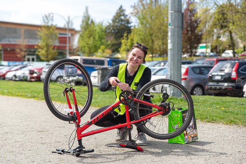 A bike education instructor kneels down and is changing the pedal of a bike that is flipped upside down. She smiles at the camera.