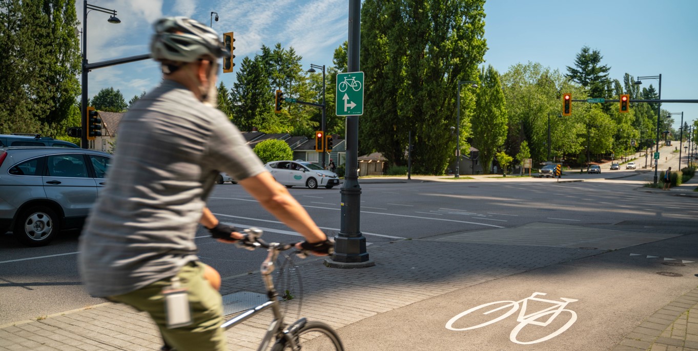 A man cycles on a separated bike path in Surrey. He is wearing a helmet, shorts, and a short sleeve shirt.