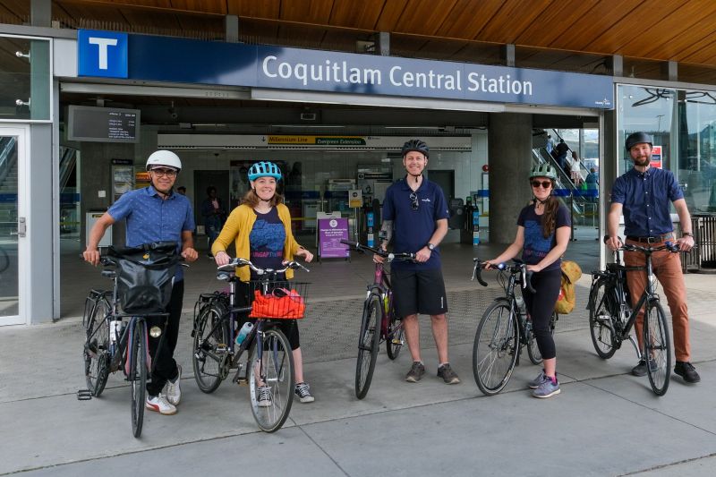 A photo of HUB Cycling and TransLink's leadership team members with their bikes in front of Coquitlam Central SkyTrain Station.