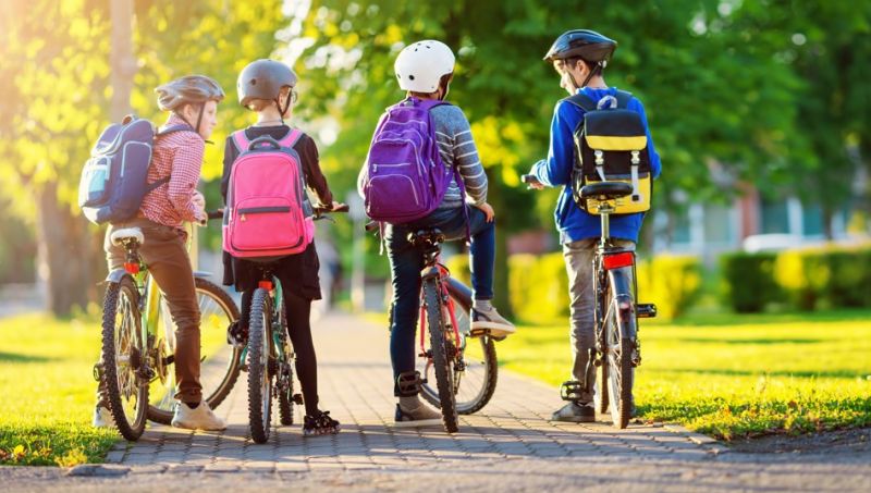 Four young students about 10 years old stand with their bikes on school grounds.