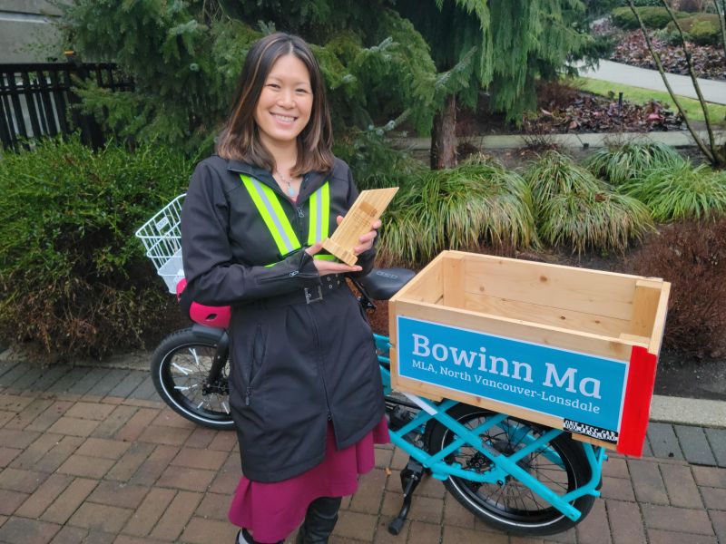 Bowinn Ma, MLA for North Vancouver-Lonsdale and the Minister of State for Infrastructure, won the 2022 Arno Schortinghuis Lifetime Achievement Award awarded by HUB Cycling at the 9th Annual HUB Bike Awards on February 24, 2022. She stands in front of her e-bike smiling and holding her award.