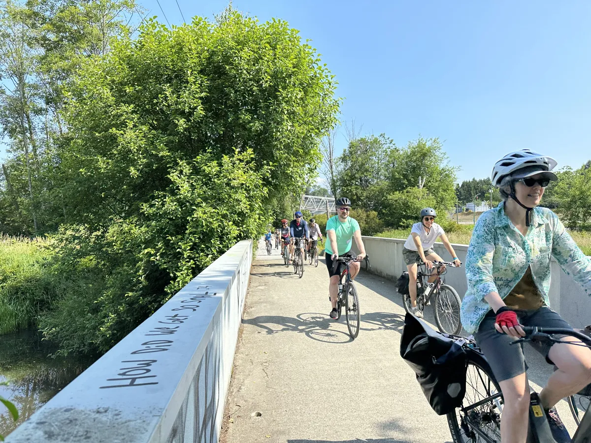 A group of people ride their bikes on a cycling path in Metro Vancouver. The weather is beautiful with blue skies.