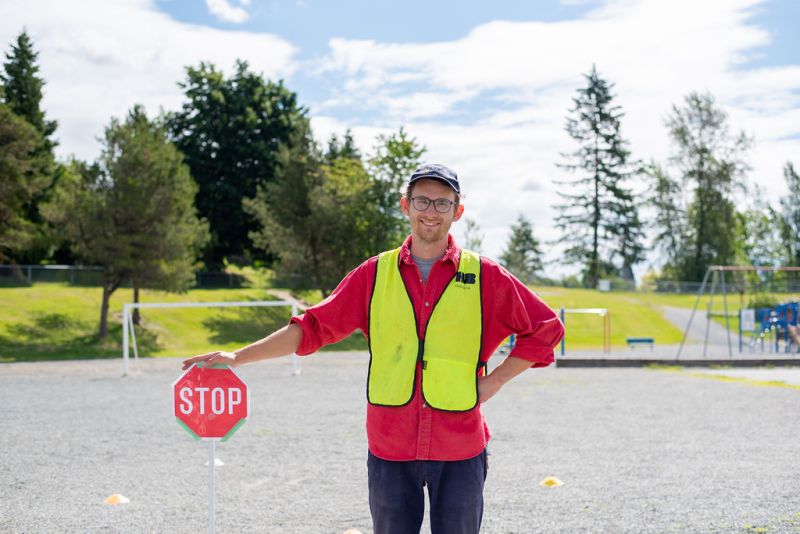 A bike education instructor smiles at the camera. He stands with his hand on top of a short 'STOP' sign.