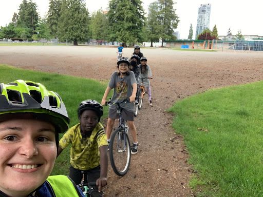 A bike education instructor holds her phone up for a selfie and captures herself and several school-aged children riding their bikes.