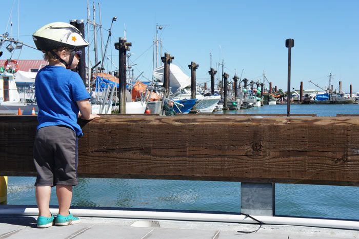 A little boy wearing a bike helmet looks at the ocean from the wharf in Steveston. Photo credit to Let's Go Biking.