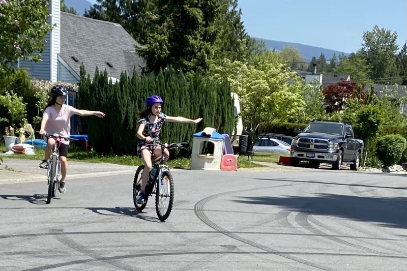 Two girls are seen making a left hand turn while riding their bikes.